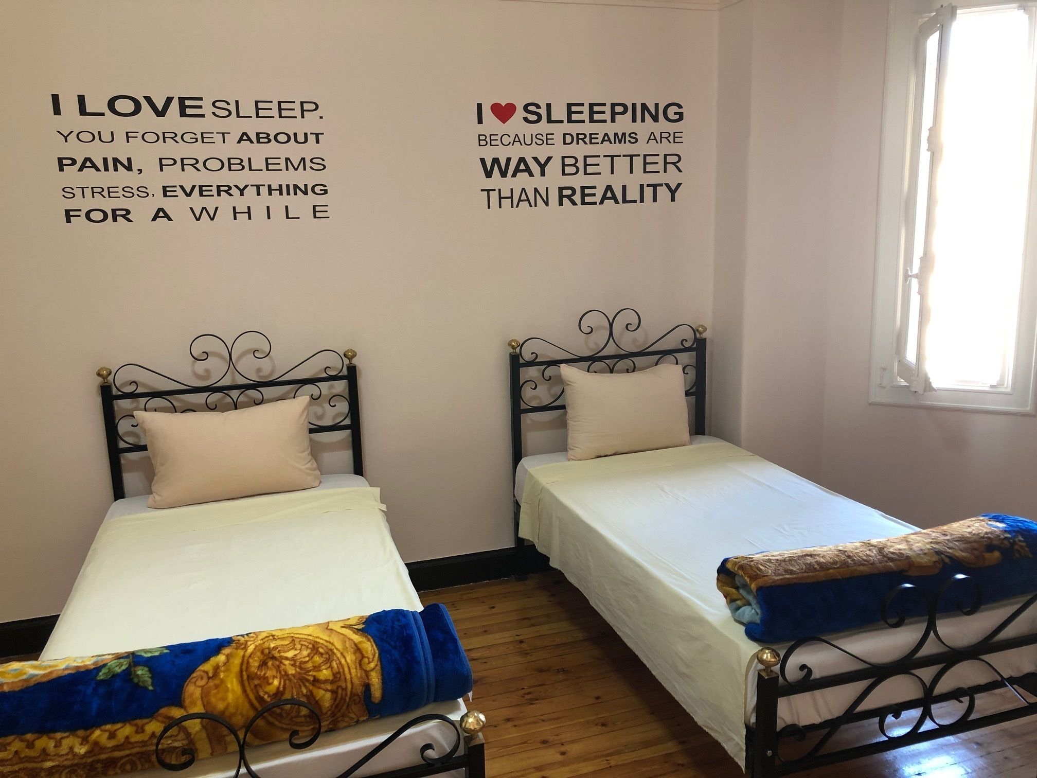 A room with two single beds, each with a decorative headboard and a pillow. The walls have motivational quotes about sleep.