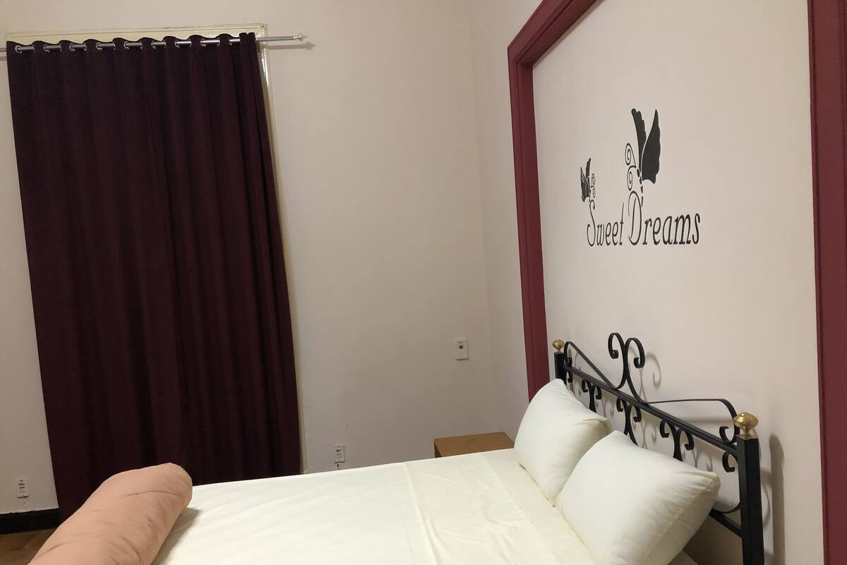 Un dormitorio con una cama, una pared con un cartel decorativo y una cortina.