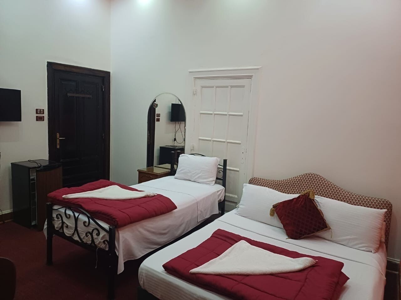 Une chambre d’hôtel avec deux lits simples, une armoire, un bureau, une chaise, un miroir et une porte.