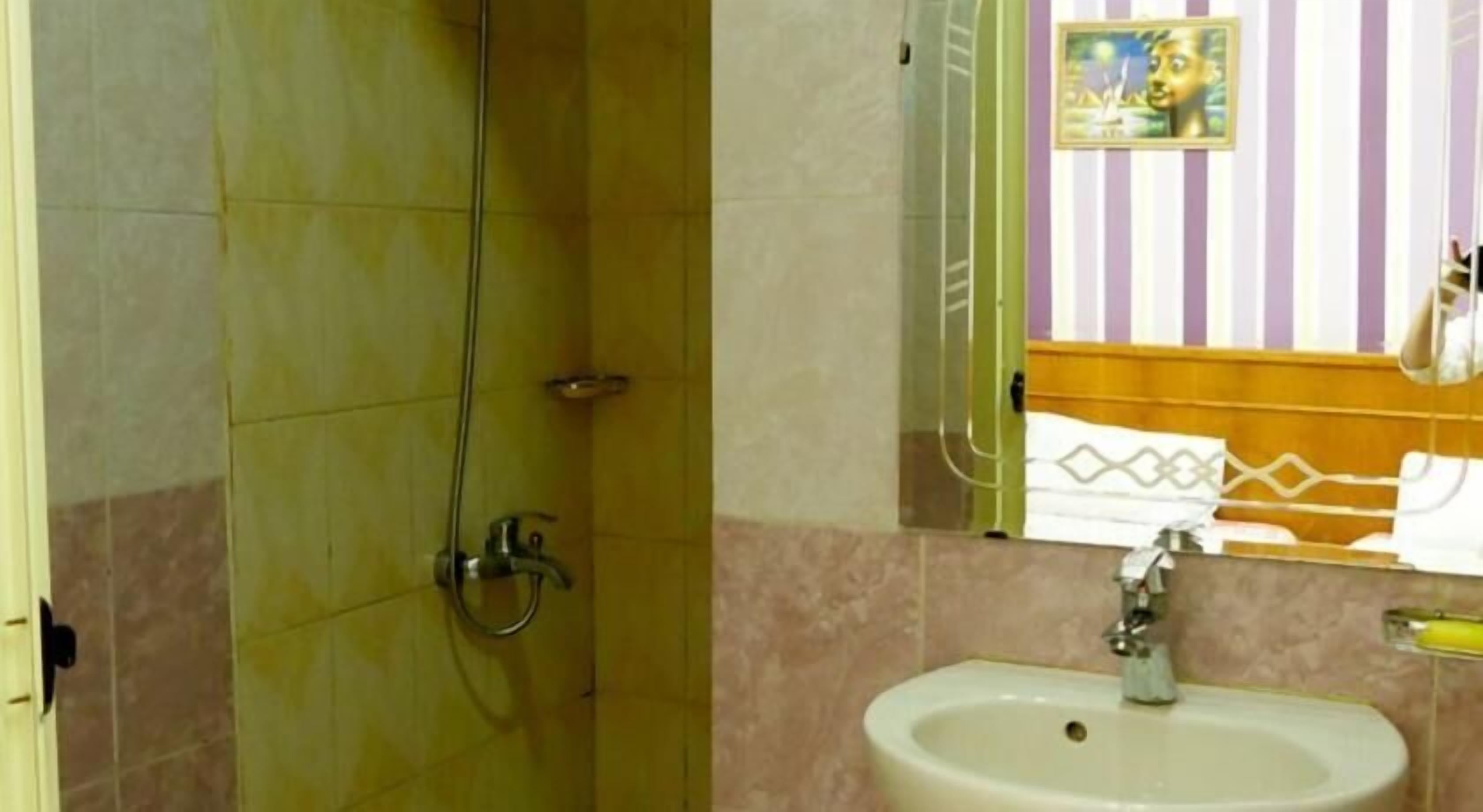 A bathroom with a shower, sink, and a mirror reflecting a striped wall and a towel rack.