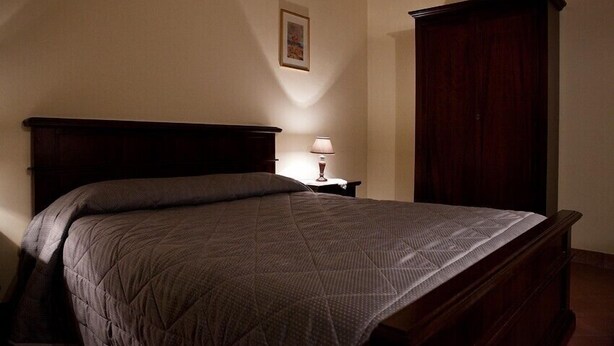 A bedroom with a bed, a nightstand, a lamp, a wardrobe, and a framed picture on the wall.