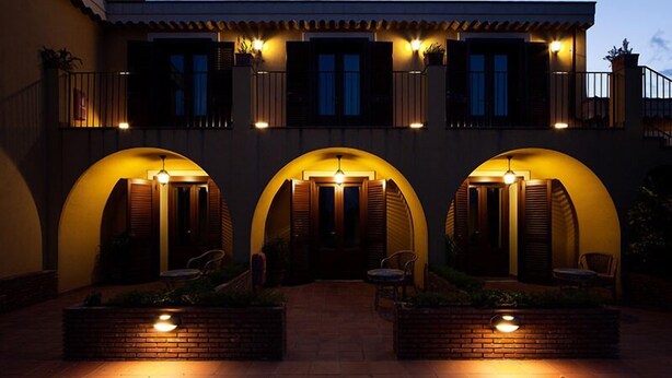 A building with three arched entrances, each with a bench and a light fixture. - La Terra del Mezzo (Riposto)