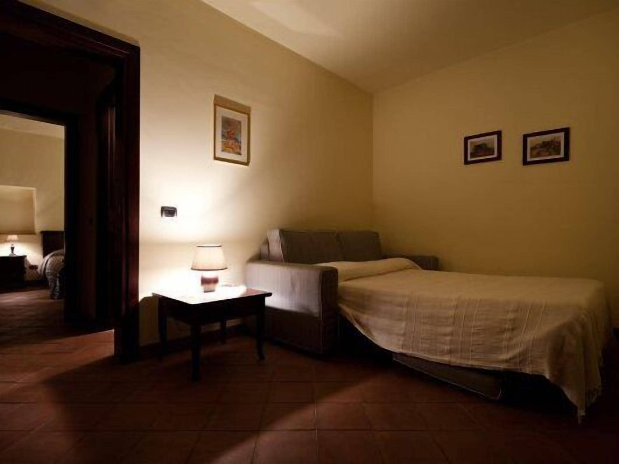 A small, dimly lit room with a single bed, a nightstand, and a chair.