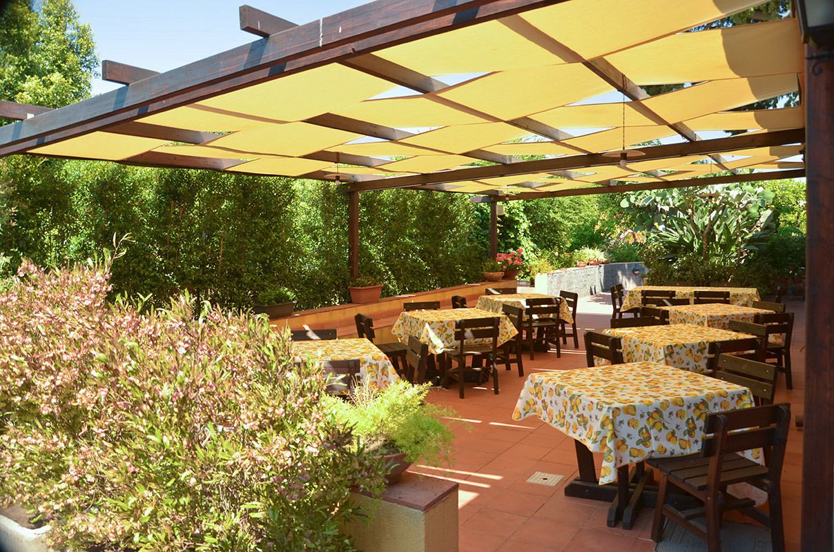 An outdoor patio area with multiple tables and chairs, covered by a yellow canopy.