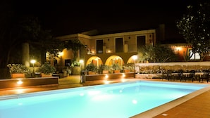 A nighttime swimming pool area with a building in the background. - La Terra del Mezzo (Riposto)
