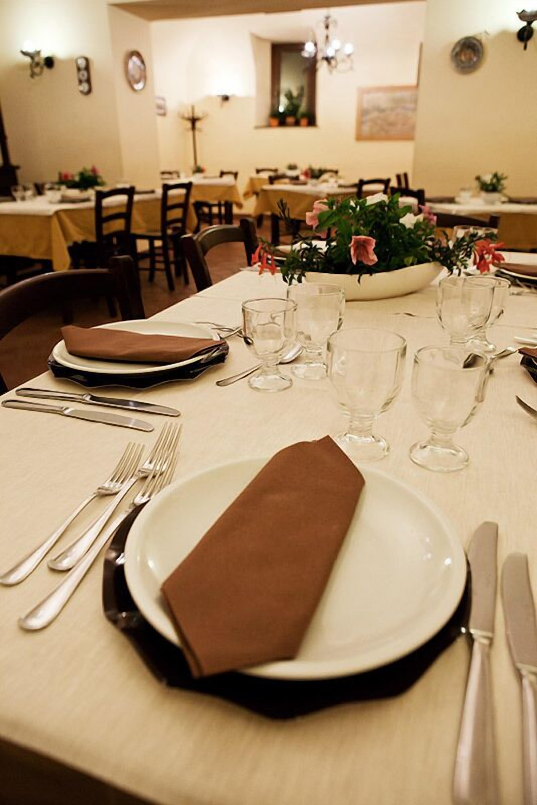 Une table à manger est dressée avec des assiettes, des couverts et des verres, et une serviette en tissu marron est pliée sur la table.
