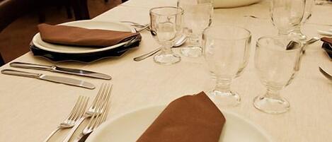 Une table à manger est dressée avec des assiettes, des couverts et des verres, et une serviette en tissu marron est pliée sur la table.