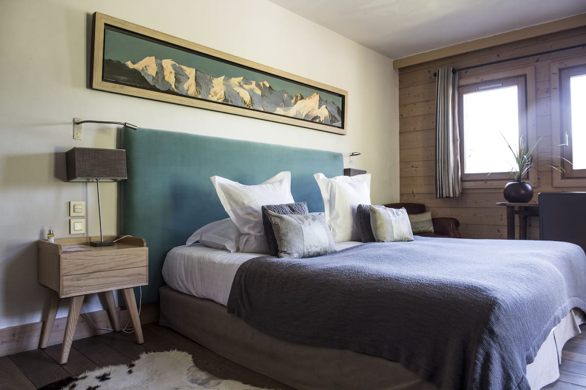 Un dormitorio con una cama grande, una mesita de noche, una lámpara, un cuadro en la pared y una ventana con cortinas.