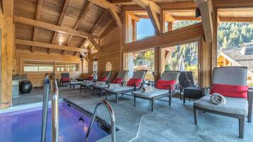 A wooden cabin with a pool, lounge chairs, and large windows offering views of the surrounding forest.
