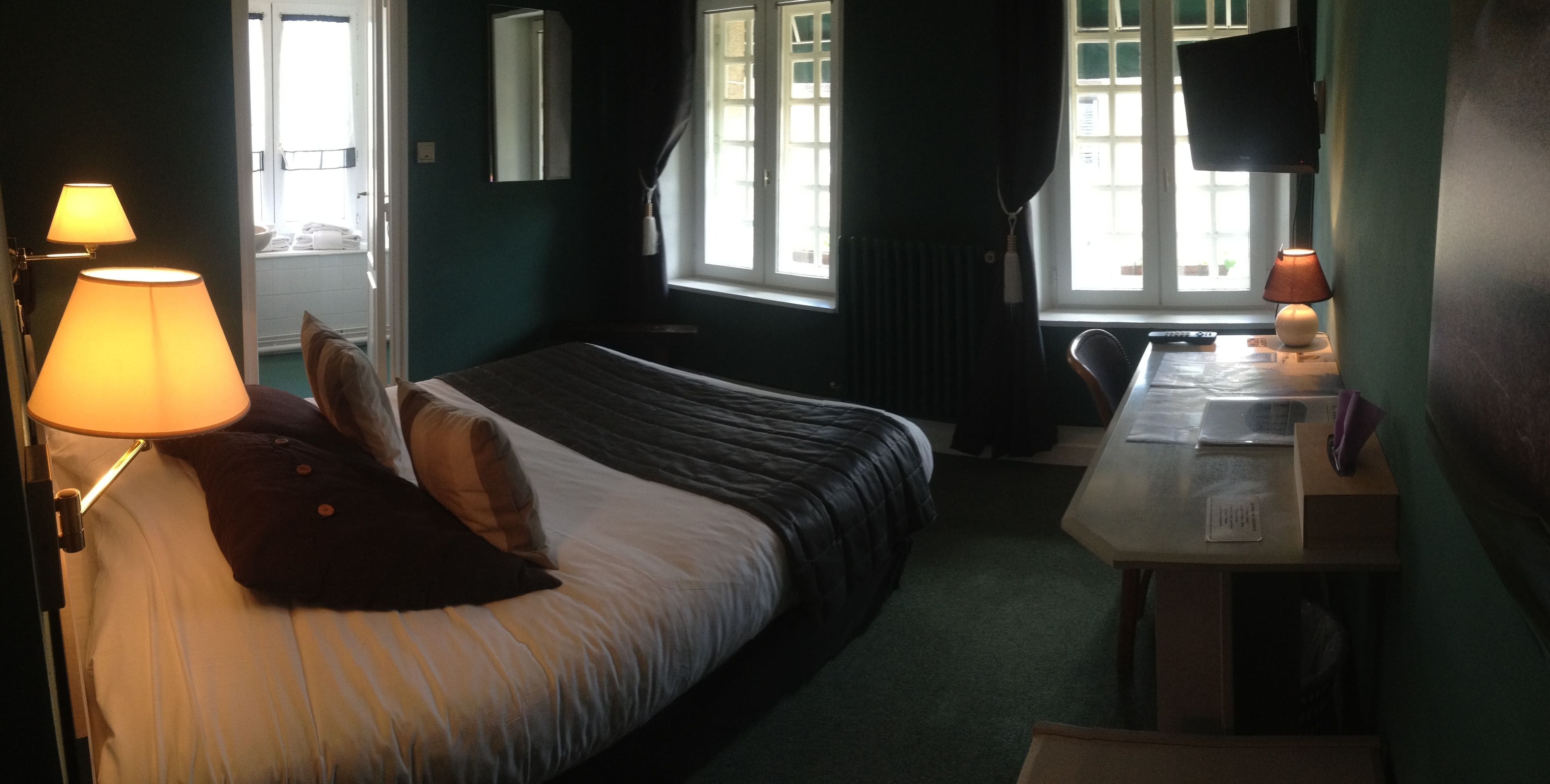 Une chambre à coucher avec un lit, des lampes de chevet, un bureau avec une lampe, une fenêtre et un radiateur.