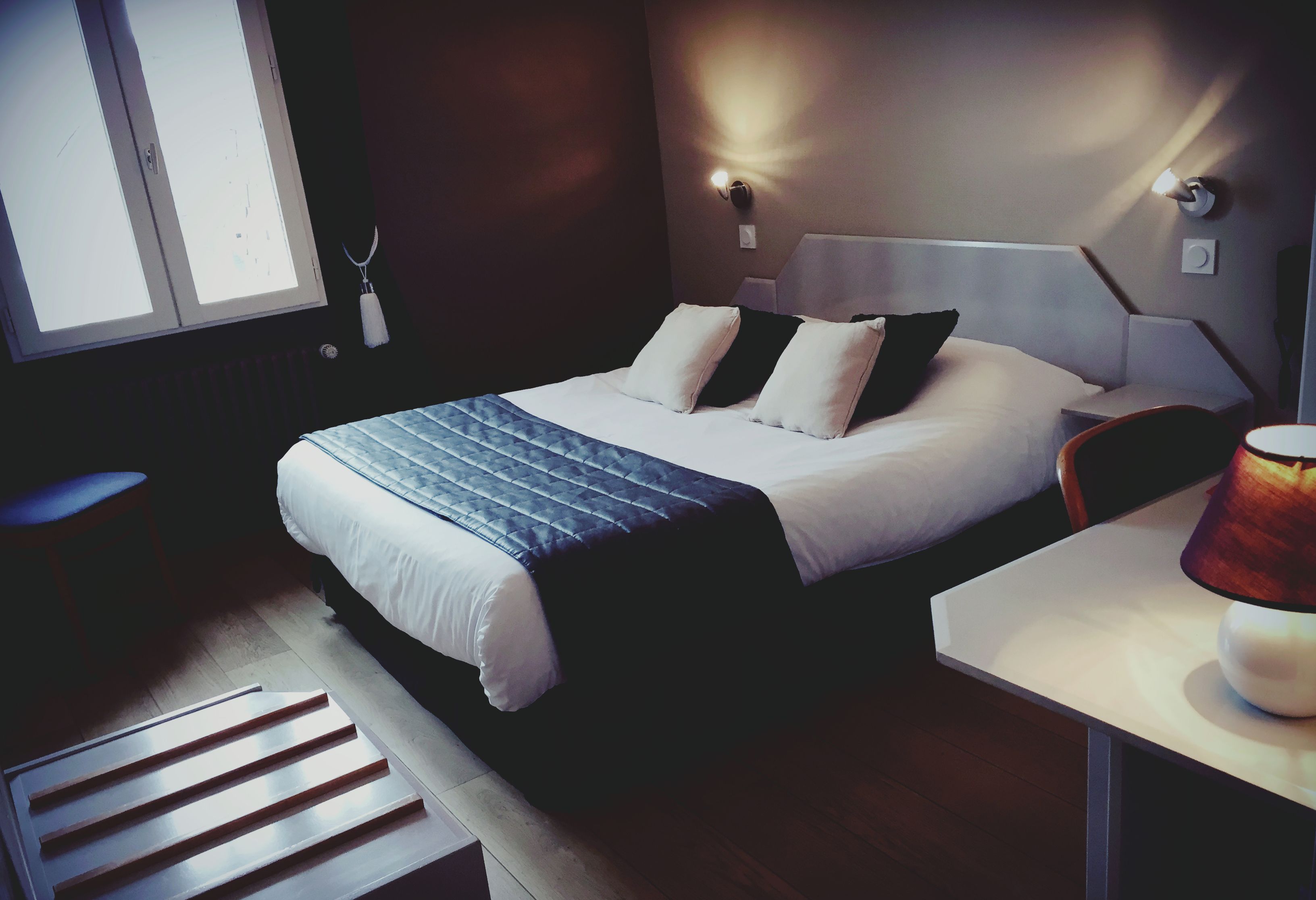 A neatly arranged hotel room with a bed, bedside table, and a chair.