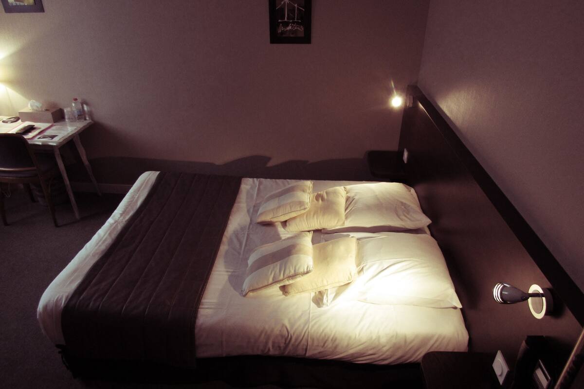 A neatly made bed with pillows and a blanket, a bedside table with a lamp, and a chair.