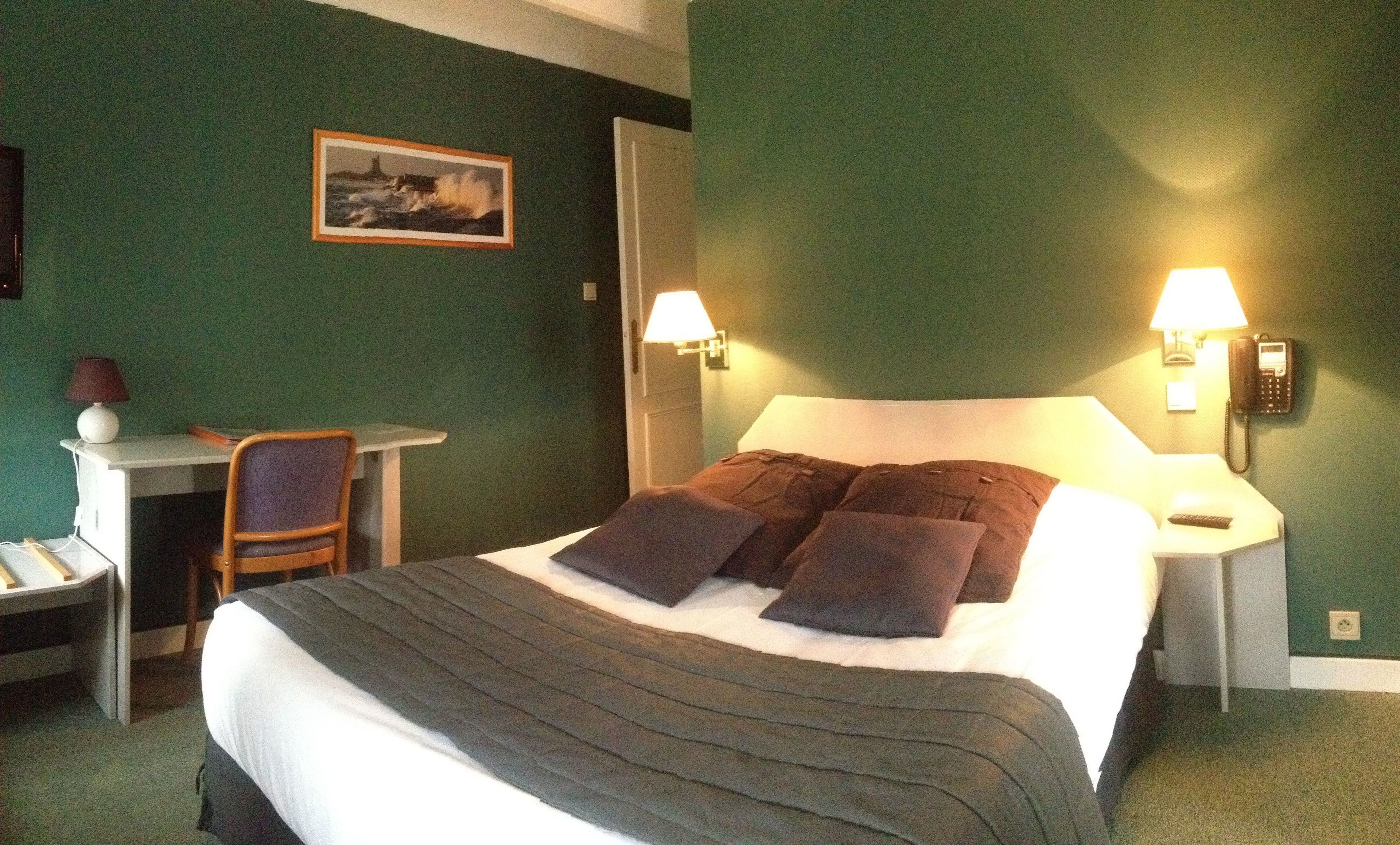 Une chambre d’hôtel avec un lit, deux lampes de chevet, un bureau avec une chaise et un tableau encadré au mur.