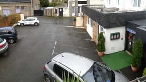 A parking lot with several cars, a building with a sign reading "ENTREE HOTEL," and a small green area with potted plants. - Hotel de la Marne (Paimpol)