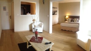 A living room with a sofa, a coffee table with a vase, a remote control, and a door leading to another room. - Hotel de la Marne (Paimpol)