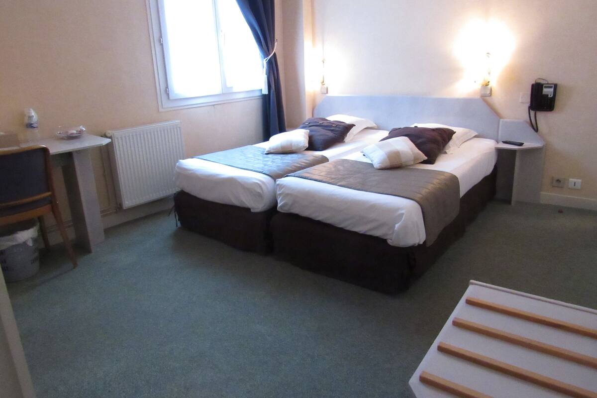 A hotel room with two beds, a desk, a chair, and a lamp.