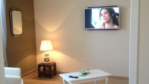 A small, neatly arranged room with a television mounted on the wall, a small table with a remote control, a lamp, and a mirror on the wall. - Hotel de la Marne (Paimpol)