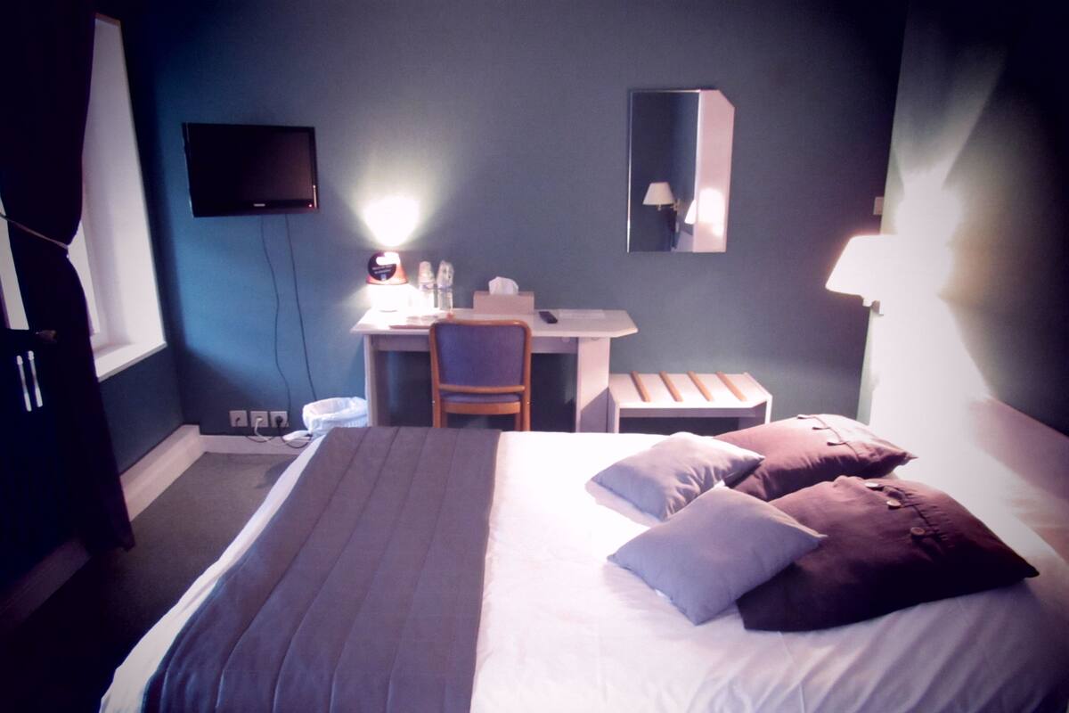 A hotel room with a bed, a desk, a chair, a TV, and a mirror.
