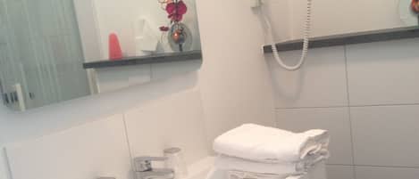 Un baño con lavamanos blanco, espejo, teléfono y un florero con flores.