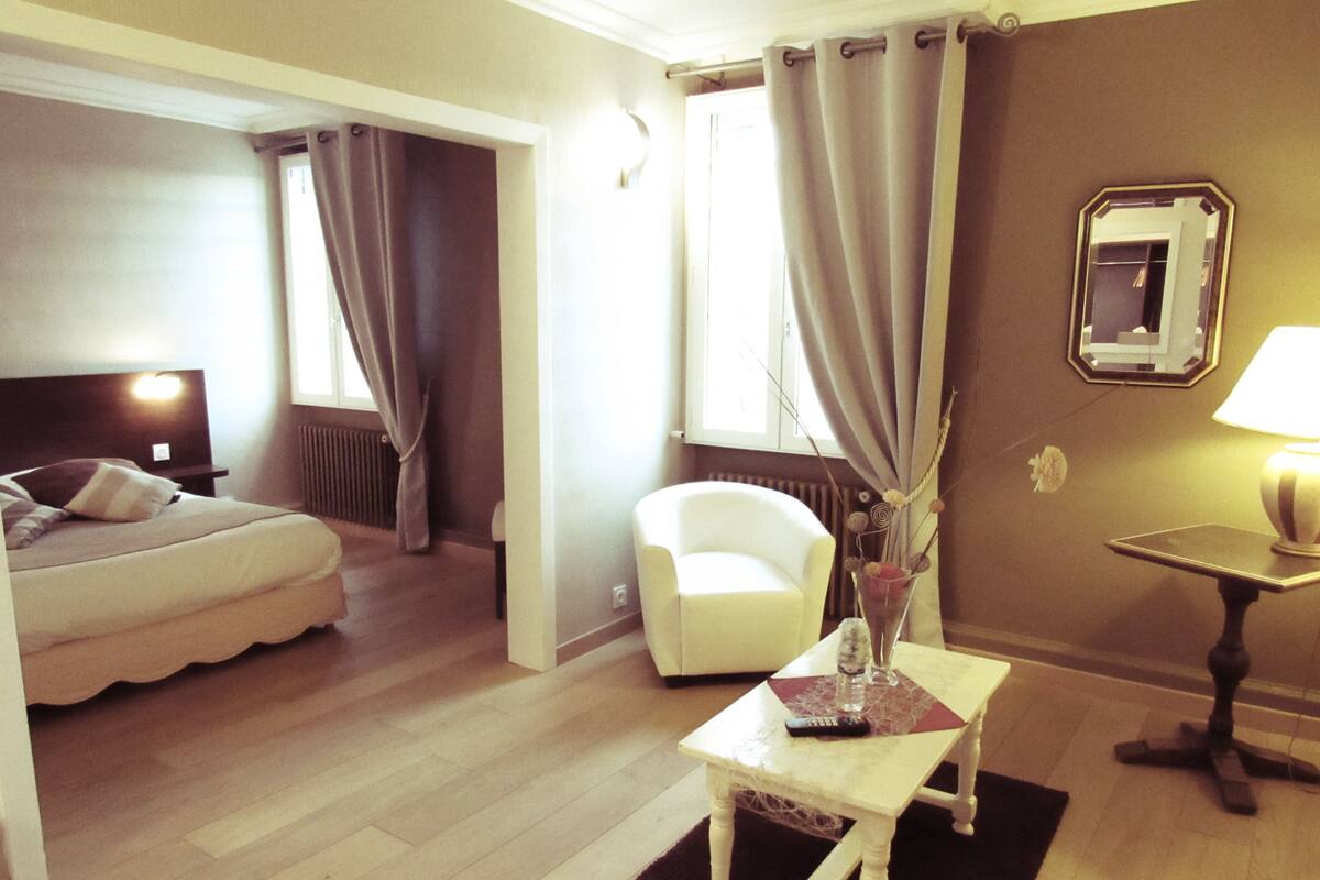 A hotel room with a bed, a chair, a small table with a lamp, and a mirror on the wall.