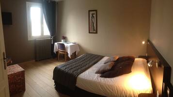 A bedroom with a bed, a desk with a chair, a radiator, and a window with curtains.