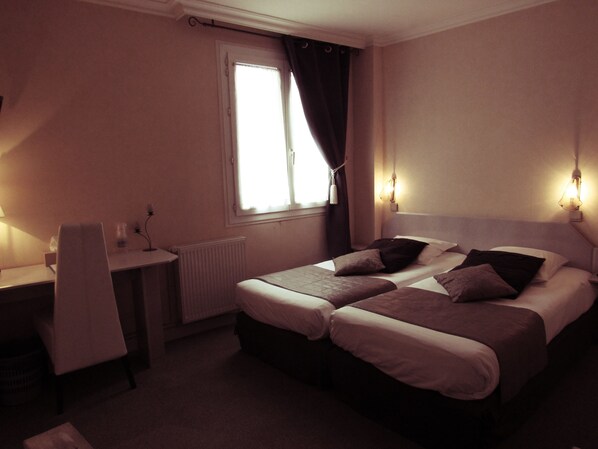 A hotel room with two beds, a desk, and a chair.