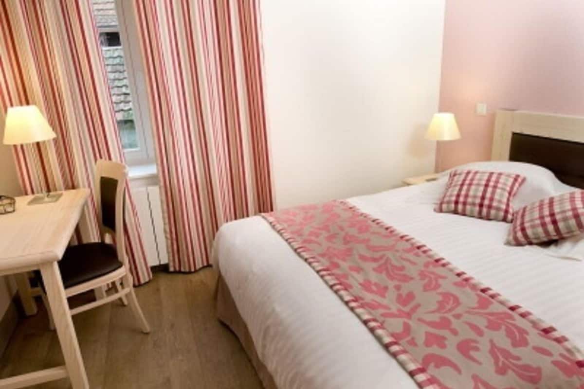 Een hotelkamer met een bed, een bureau, een stoel en een raam met gordijnen.