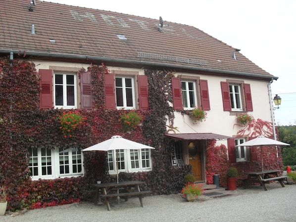 A building with red shutters, a gravel driveway, and outdoor seating.