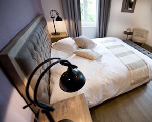 A neatly made bed with a headboard, a bedside lamp, and a window with curtains.