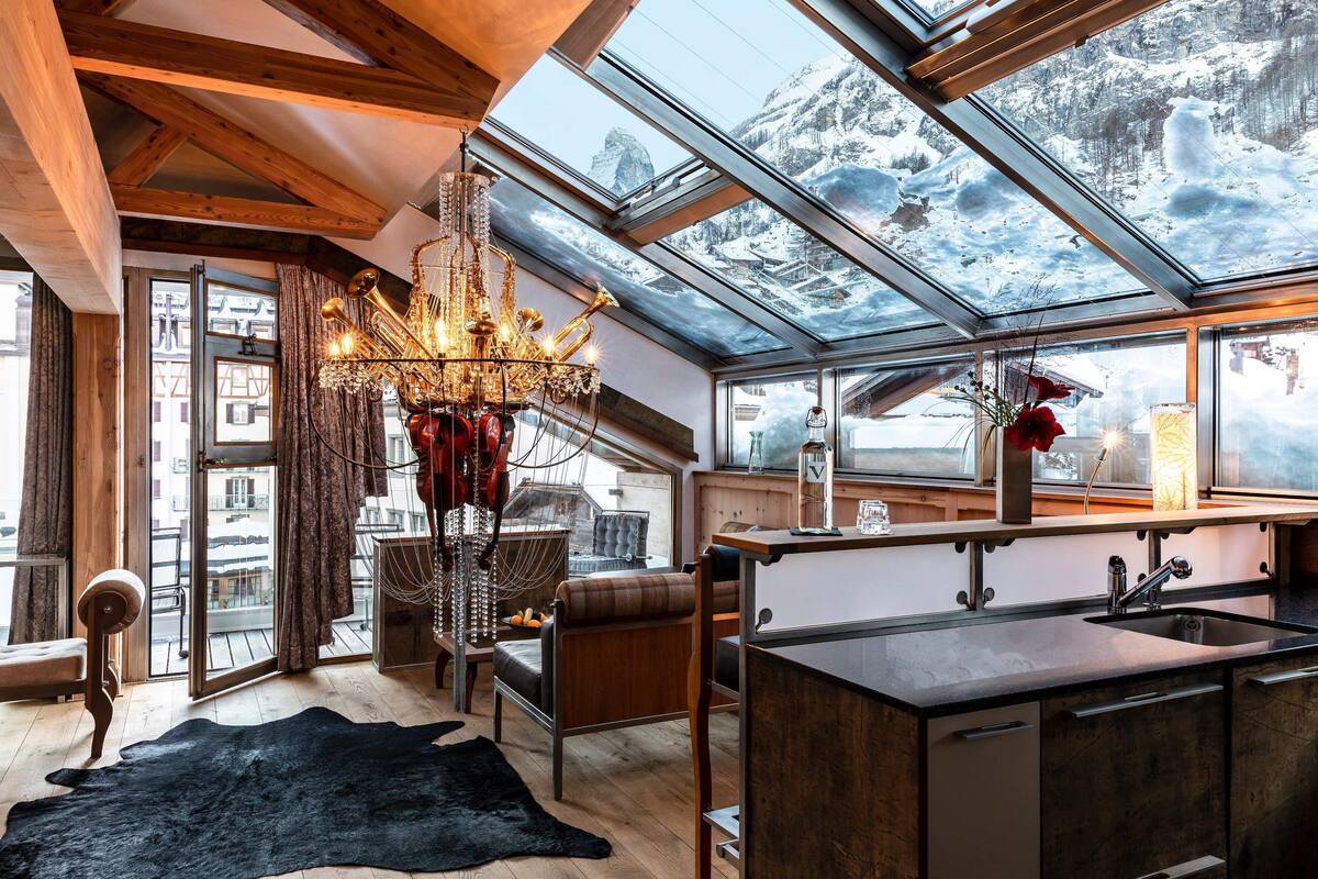 A modern kitchen with a large window, a chandelier, and a view of snowy mountains.