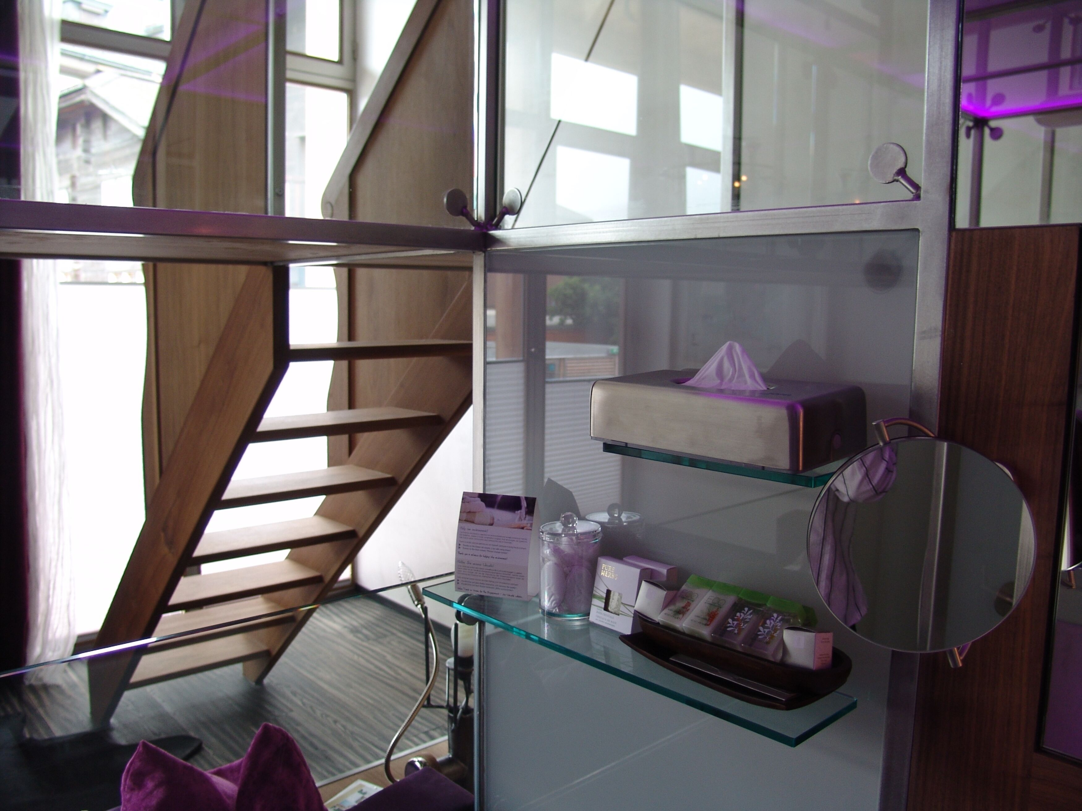 A modern bathroom with a glass shower enclosure, a wooden staircase, and a glass shelf with toiletries.