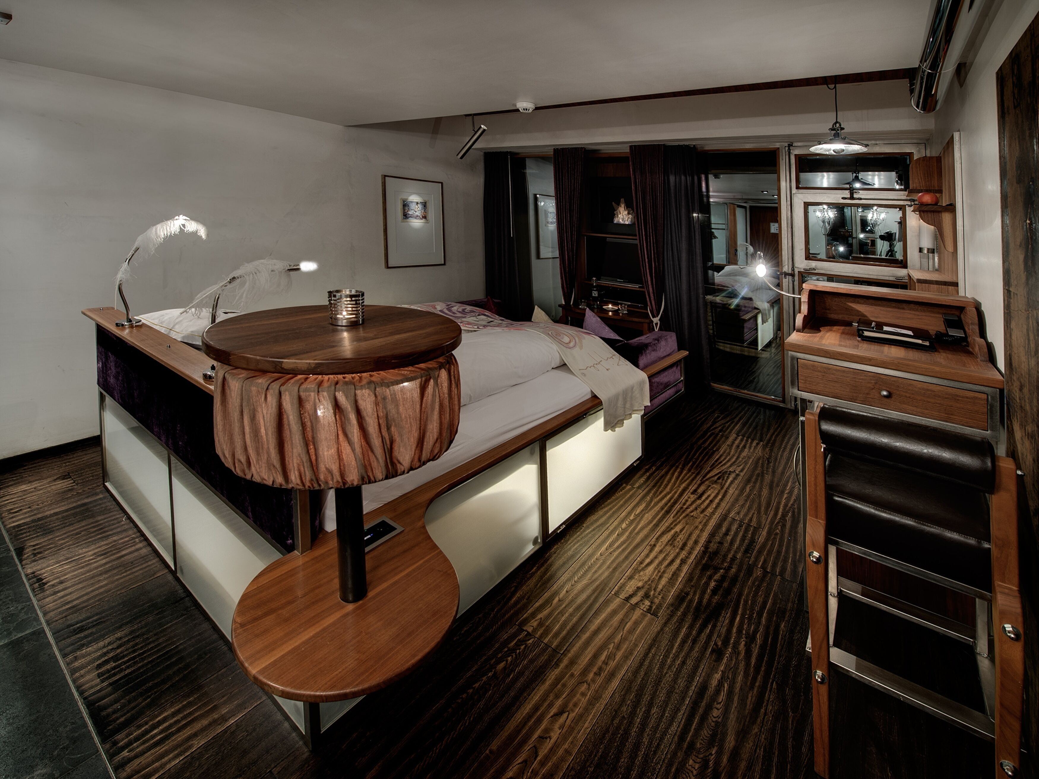 Una habitación de hotel moderna con una cama, una mesita de noche y una pequeña mesa redonda con una lámpara.