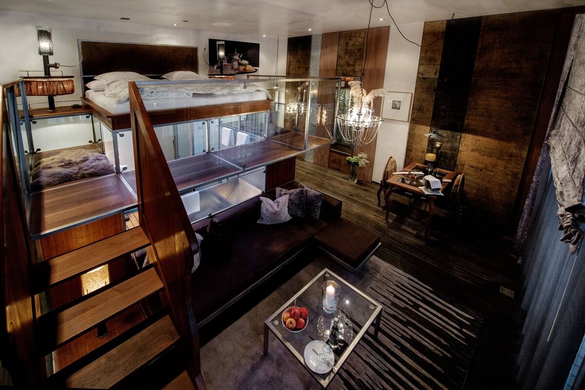 A modern loft bedroom with a bunk bed, a glass dining table with a candle, and a cozy seating area.