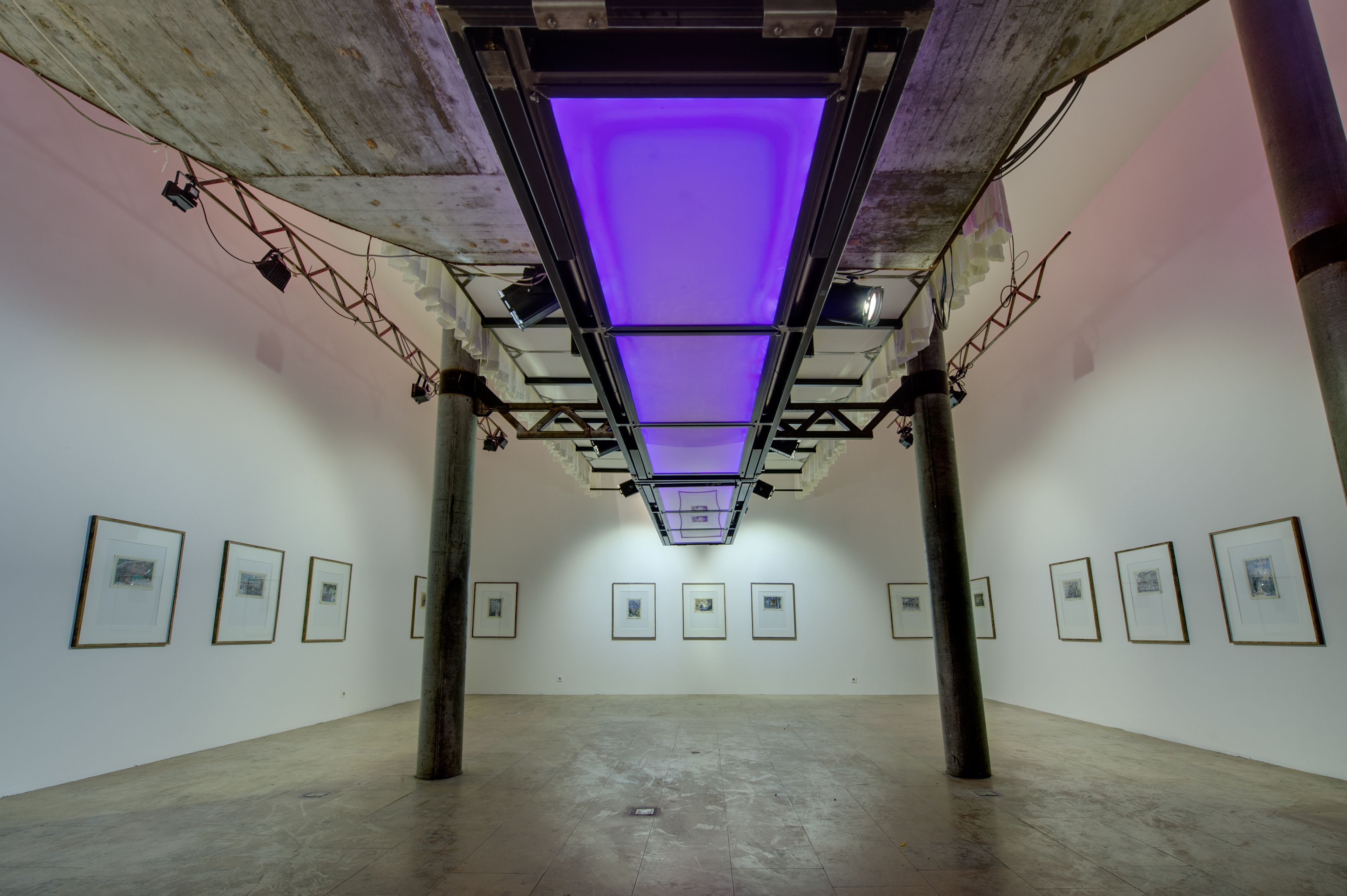 An art gallery with a central ceiling light and framed artworks on the walls.