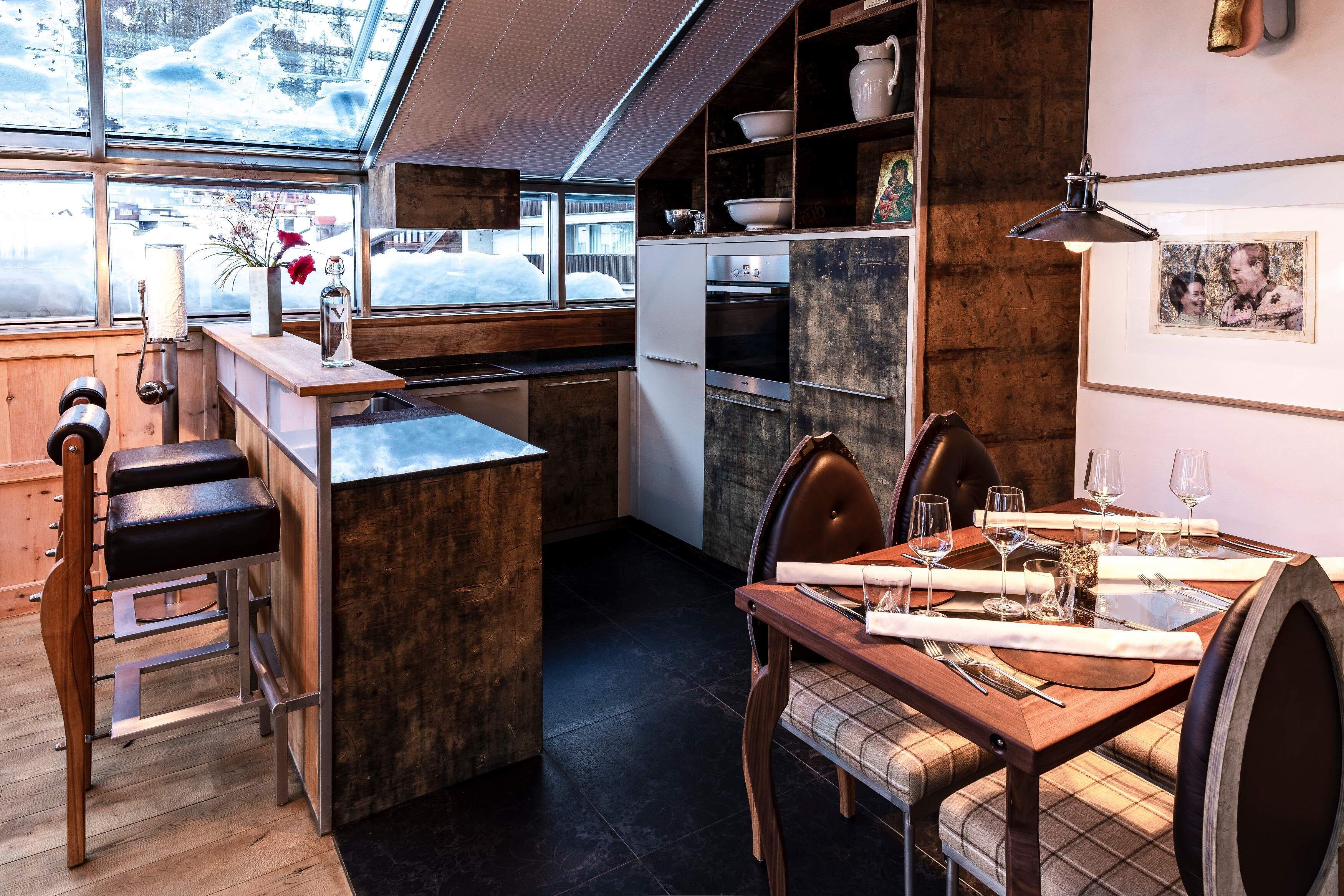 A modern kitchen with a wooden island, a dining area with a table set for four, and a large window with a view of snow outside.