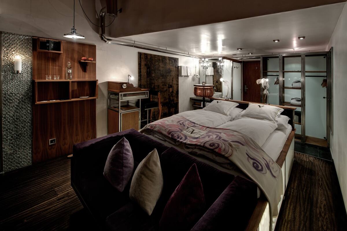 A modern bedroom with a large bed, wooden shelving, a vanity, and a walk-in closet.