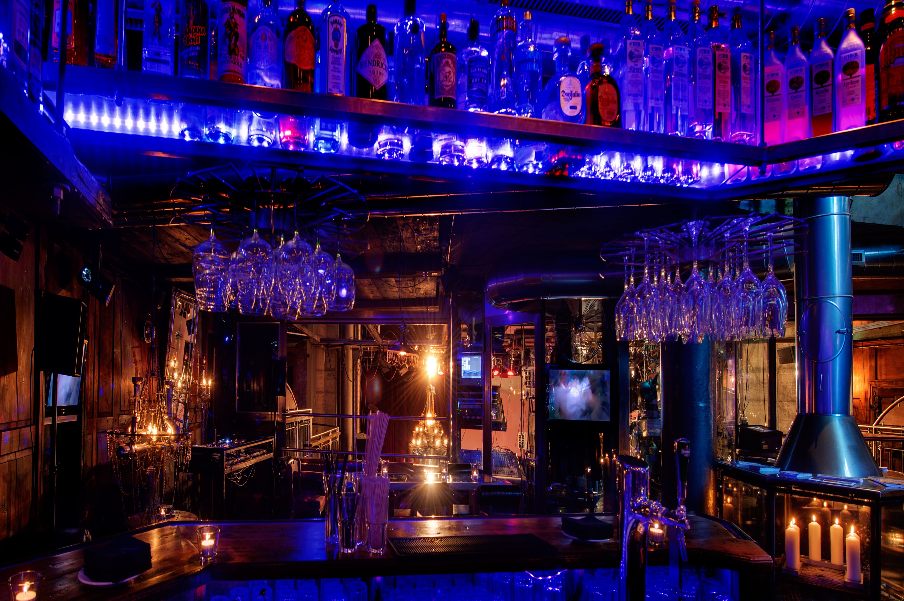 A bar with a variety of liquor bottles, hanging glassware, and candles.