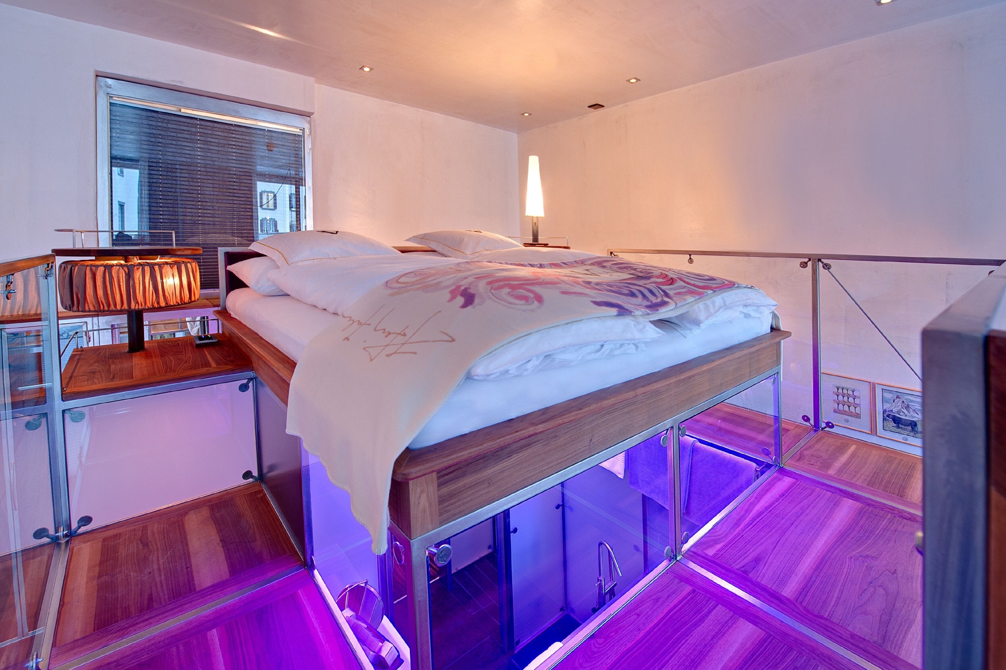 Un dormitorio moderno con cama, mesita de noche, lámpara y vista a la ciudad a través de una ventana.