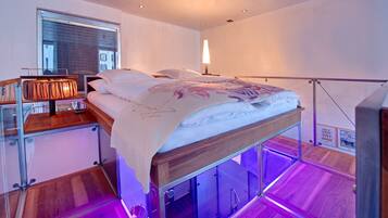 Un dormitorio moderno con cama, mesita de noche, lámpara y vista a la ciudad a través de una ventana.