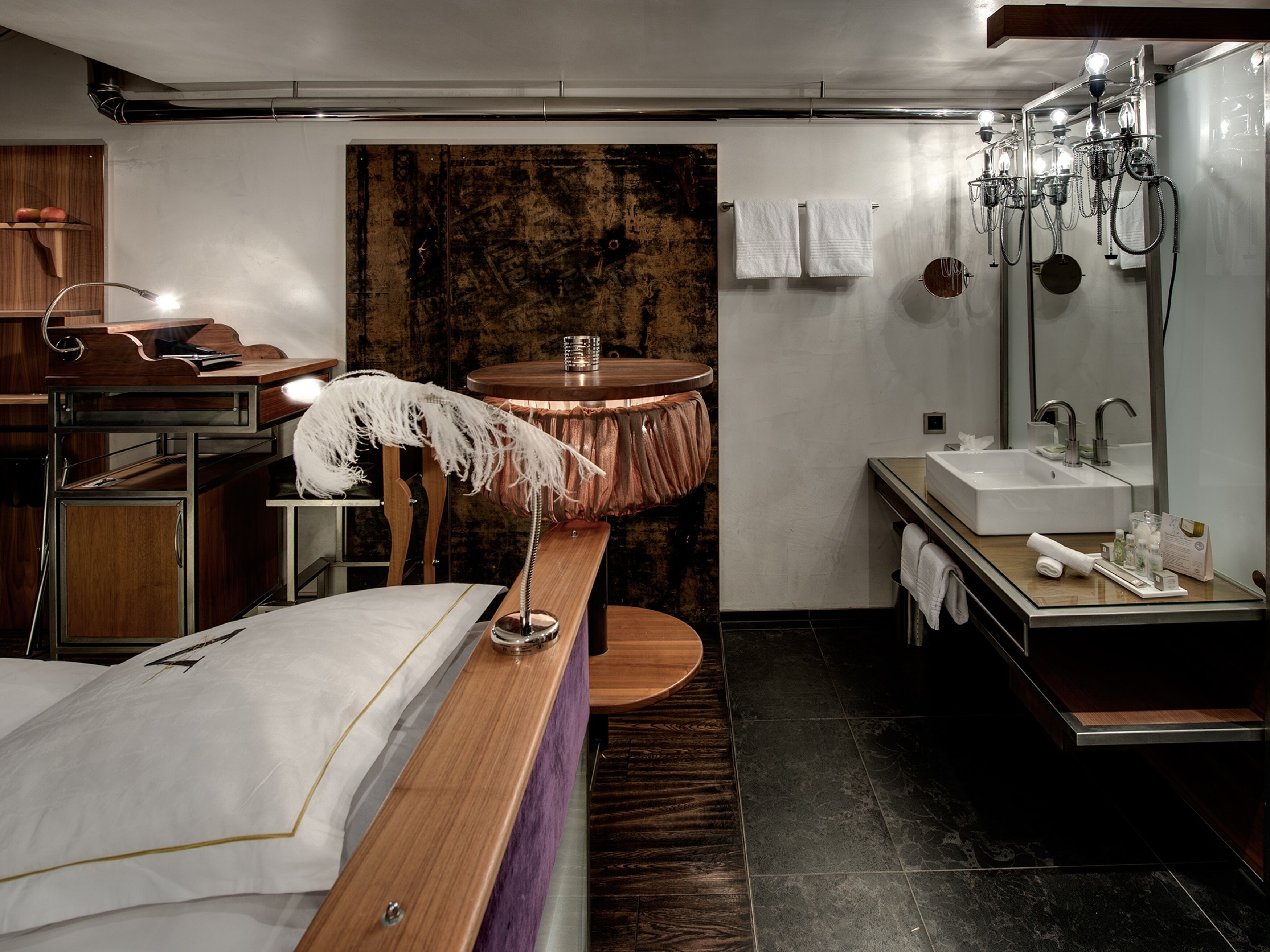 Una habitación de hotel moderna con una cama de madera, una mesa redonda, un espejo grande, un lavamanos y un perchero para toallas.