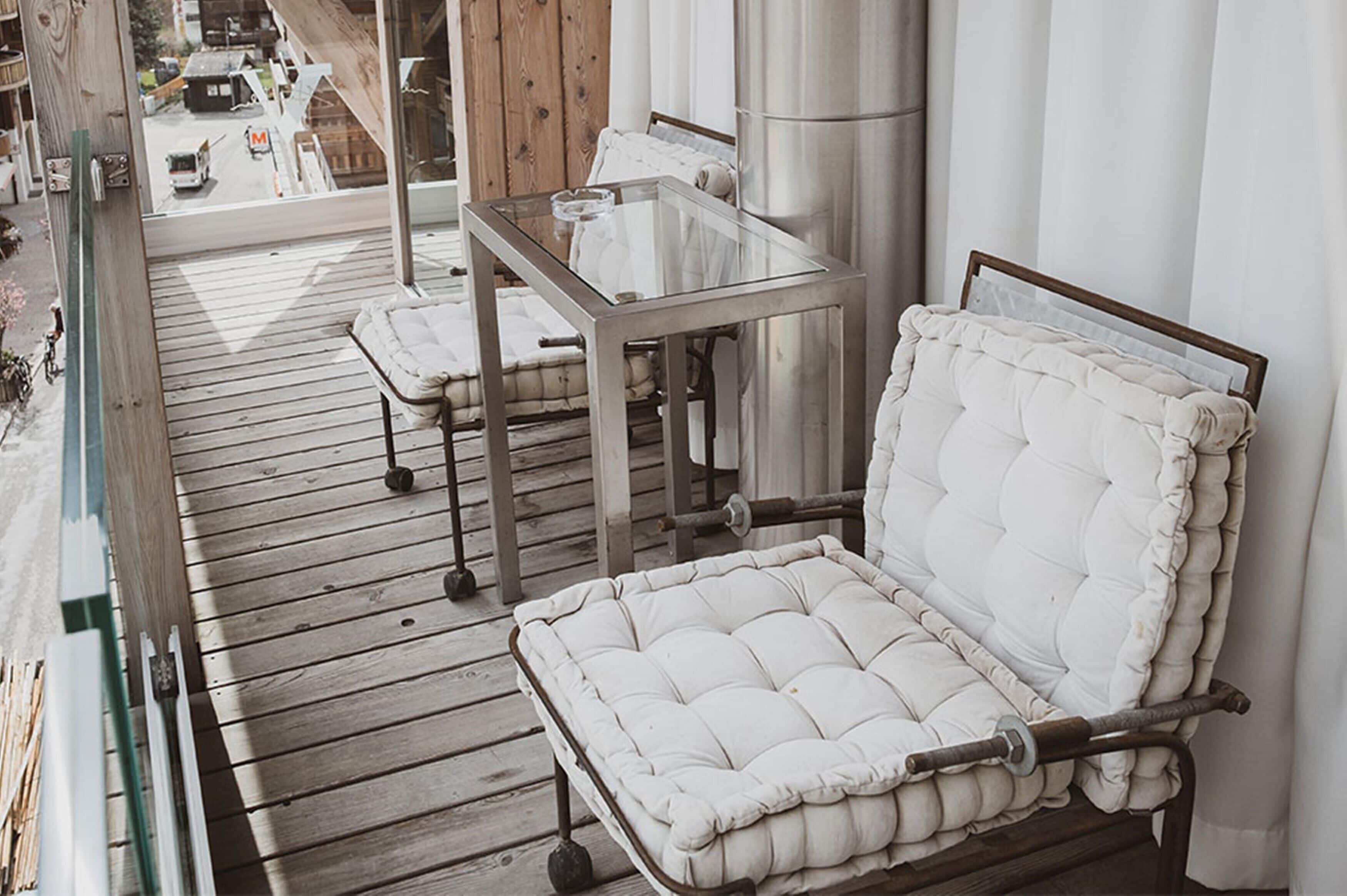A balcony with a cushioned chair, a glass-top table, and a view of the street.