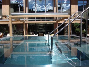A glass-enclosed pool with metal railings and a wooden deck area.