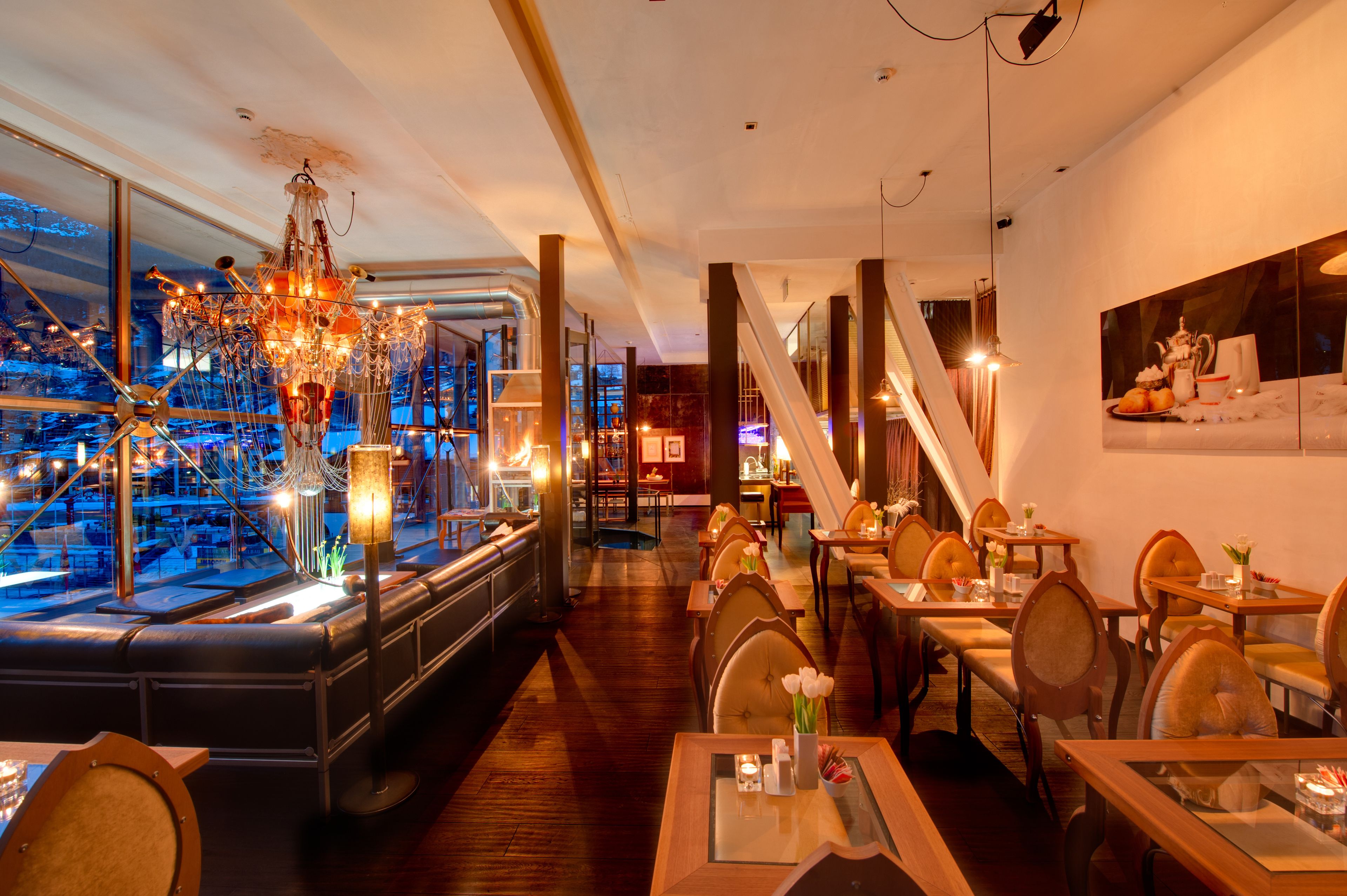 Ein Restaurant mit Barbereich, Holztischen und -stühlen. Eine Kristallleuchter ist vorhanden und es gibt einen Blick auf die Stadt durch große Fenster.