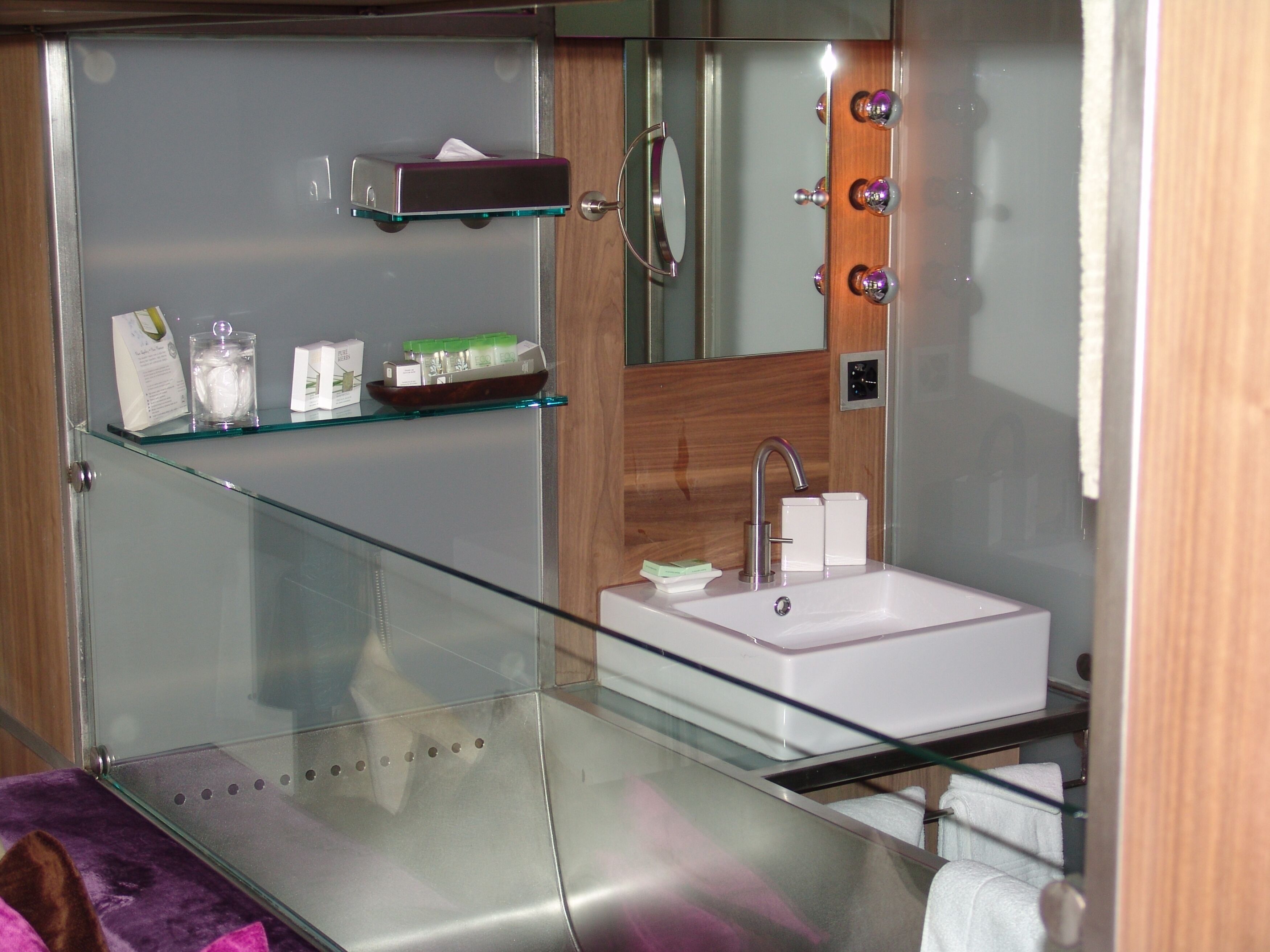 Een moderne badkamer met een glazen plank, een witte wastafel en een spiegel met verlichting.