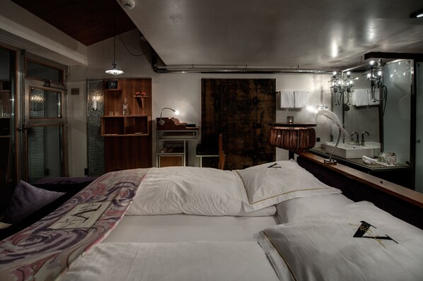 A hotel room with a large bed, a wooden dresser, a vanity with a mirror, and a large window.