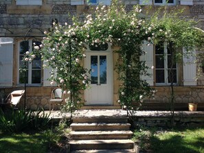 Un bâtiment en pierre avec une porte blanche, un petit porche et des marches menant à l’entrée.