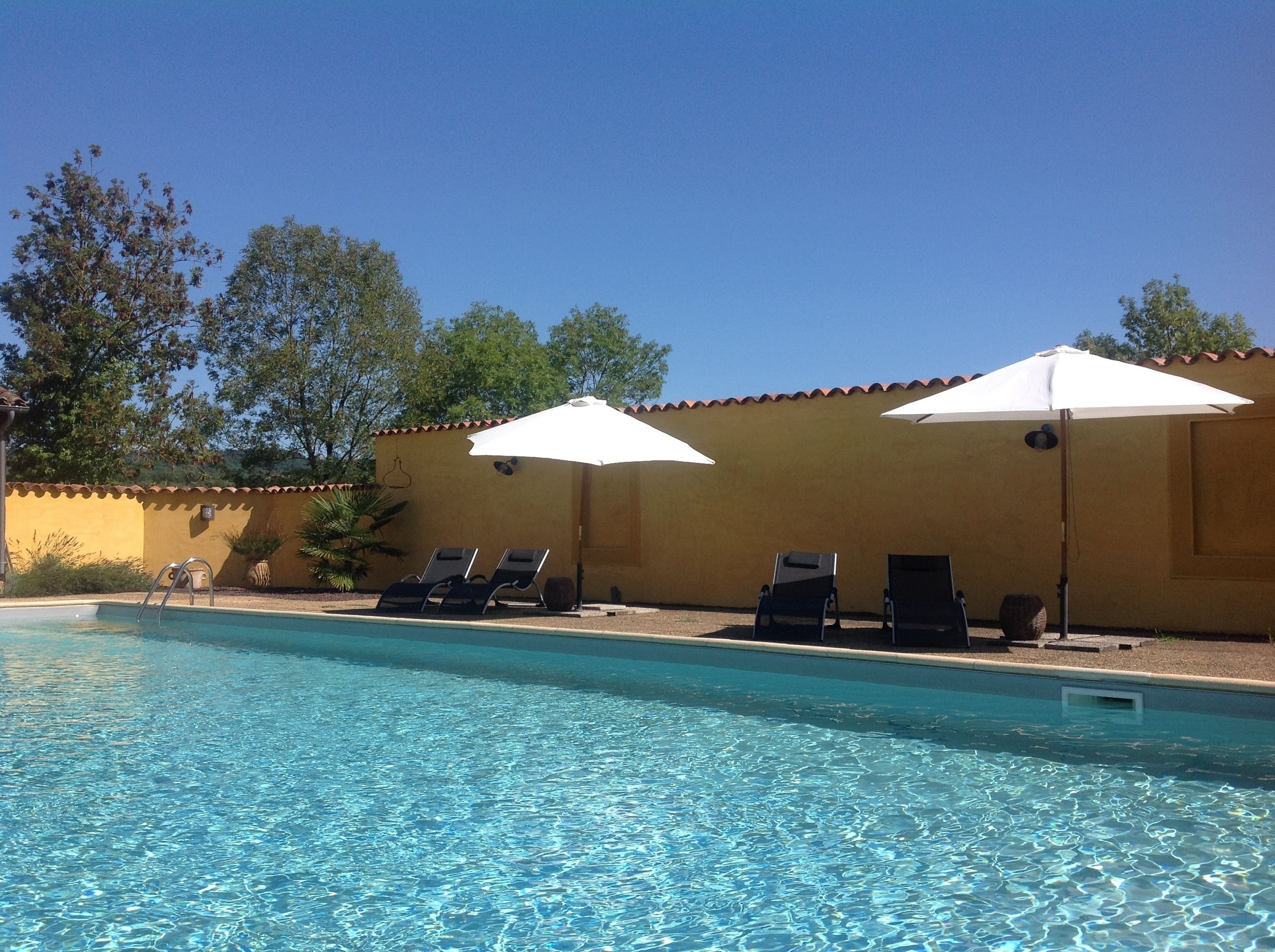 A pool area with lounge chairs and umbrellas, surrounded by a yellow wall and trees.
