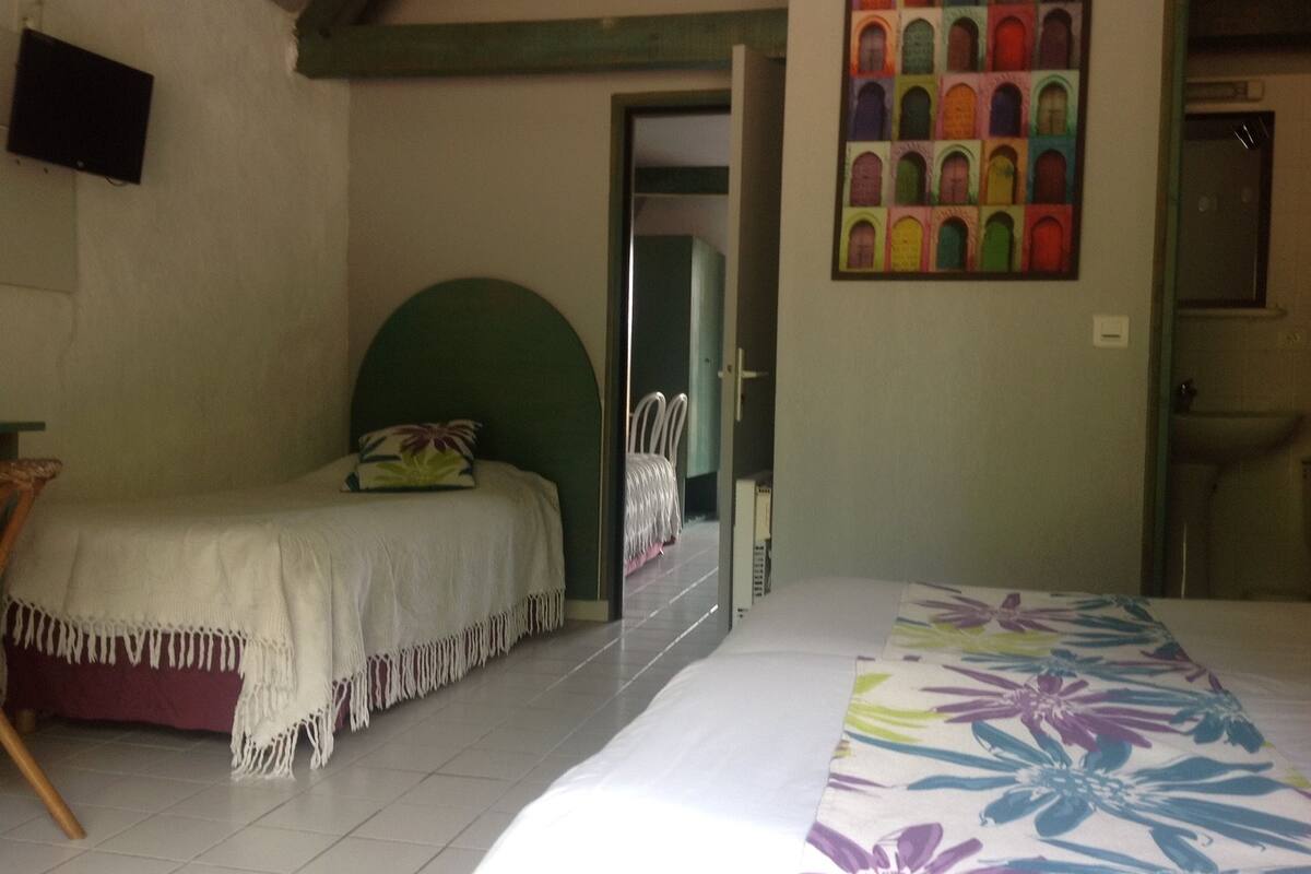 Un dormitorio con cama, una silla, una puerta y un baño visible a través de una puerta abierta.