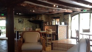 Ein rustikales Interieur mit freiliegenden Holzbalken, Korbmöbeln und einem Kamin aus Ziegelsteinen.