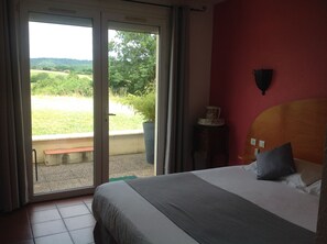Une chambre d’hôtel avec un lit, une petite table agrémentée d’un objet décoratif, et une vue sur un paysage verdoyant par une porte coulissante.